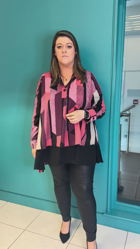 A video of a plus size woman wearing a striking graphic stripe and structured stand-up collar blouse with leather look leggings and black court shoes.