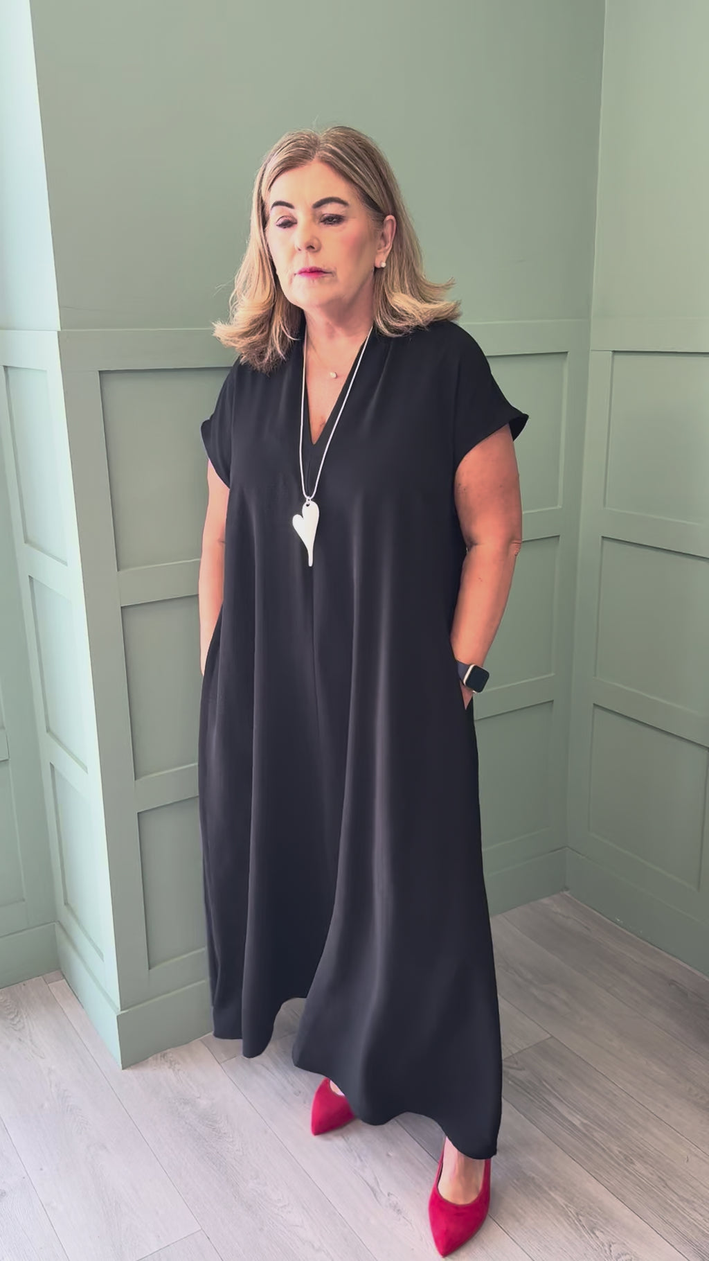 A video of a curvy woman wearing a black short sleeve maxi dress with red court shoes.