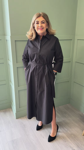 A video of a plus size woman wearing a black dress with a white stripe along the side and black court shoes.