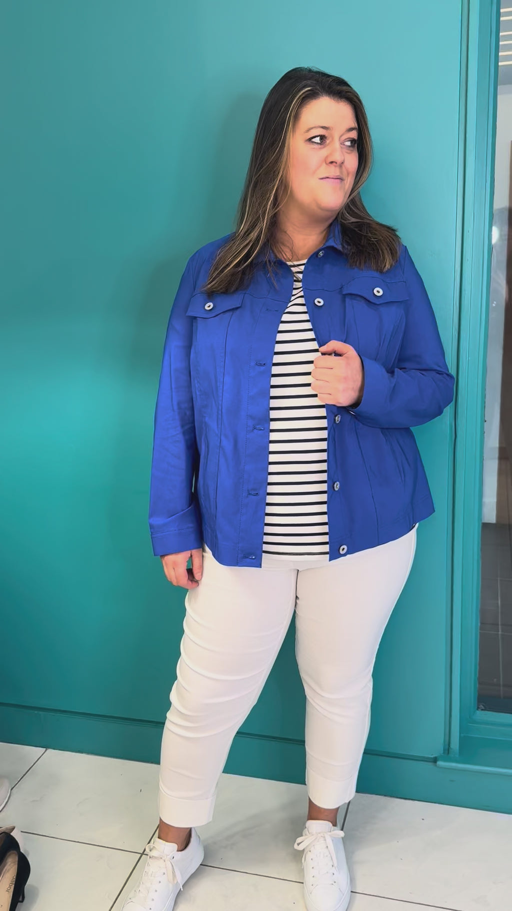 A video of a plus size woman wearing a blue denim style jacket over a striped t-shirt with and white cropped trousers.